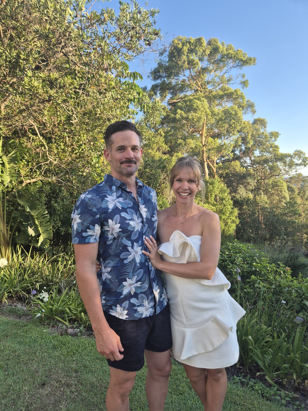 Sally and her husband dressed up in a lush green garden