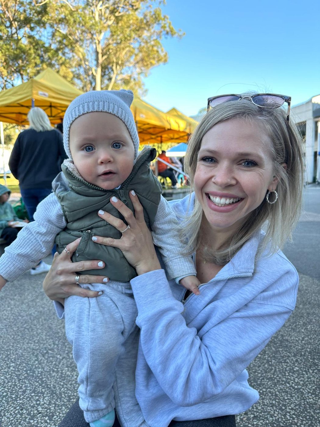 Sally smiling while holding her youngest at a sunny outdoor market